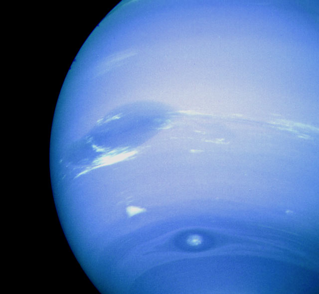 Neptune’s Great Dark Spot, accompanied by white high-altitude clouds.